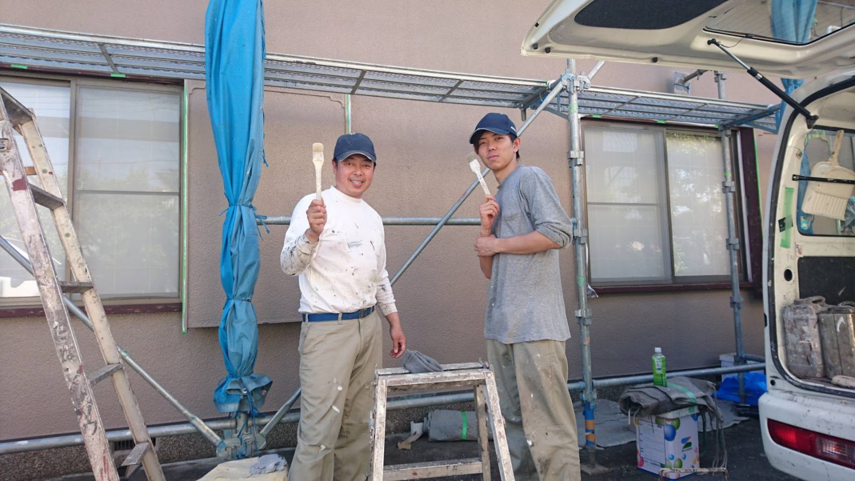 足場の前で刷毛を持つ職人2名